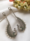 Both peacock ear cuff earrings displayed on white cloth with chain hooks and floral background
