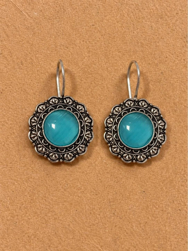 Pair of oxidised silver floral drop earrings with turquoise cat-eye cabochon on a cork surface