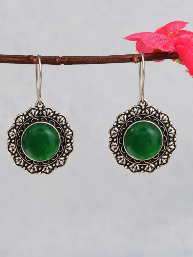 Pair of oxidised silver circular drop earrings with green cabochon centre hanging from a wooden branch