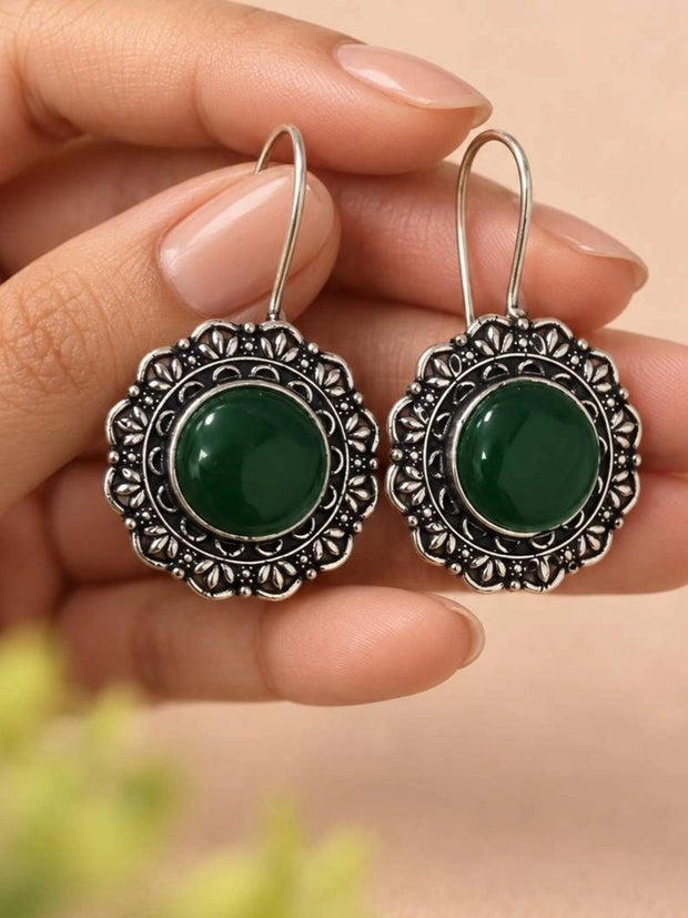 Both oxidised silver green stone circular drop earrings held flat in a woman's palm showing floral border detail