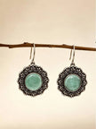 Pair of oxidised silver circular drop earrings with mint green cabochon hanging from a wooden branch