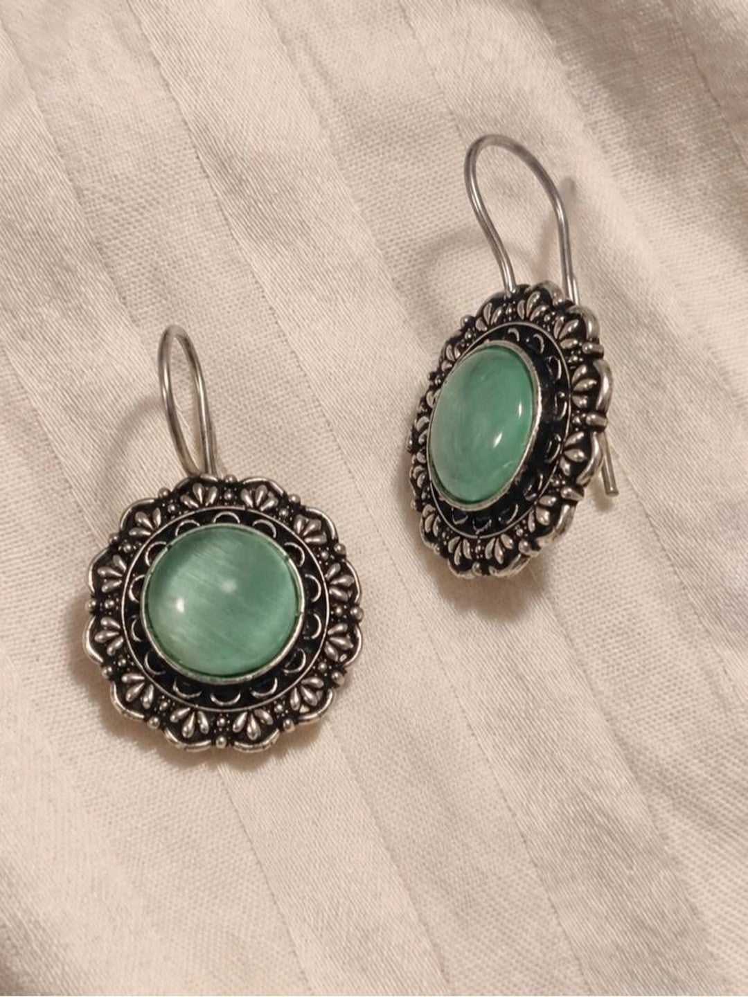 Front and side view of oxidised silver circular drop earrings laid on white fabric