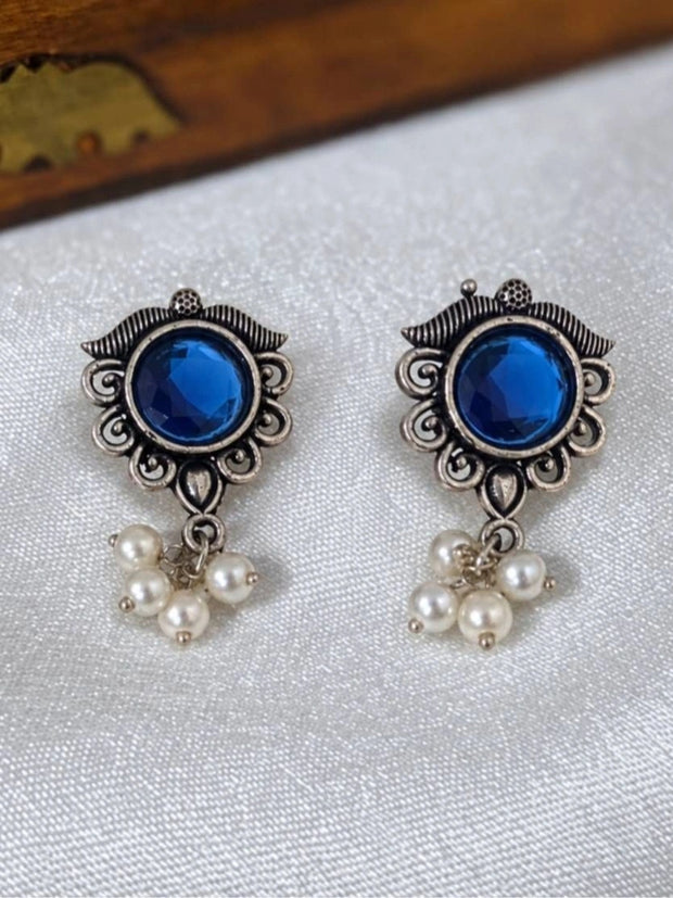 Pair of oxidised silver floral stud earrings with cobalt blue centre stone and pearl drops laid flat