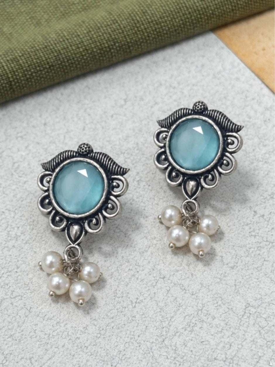 Pair of oxidised silver filigree studs with teal cabochon and faux pearl cluster drops on grey surface