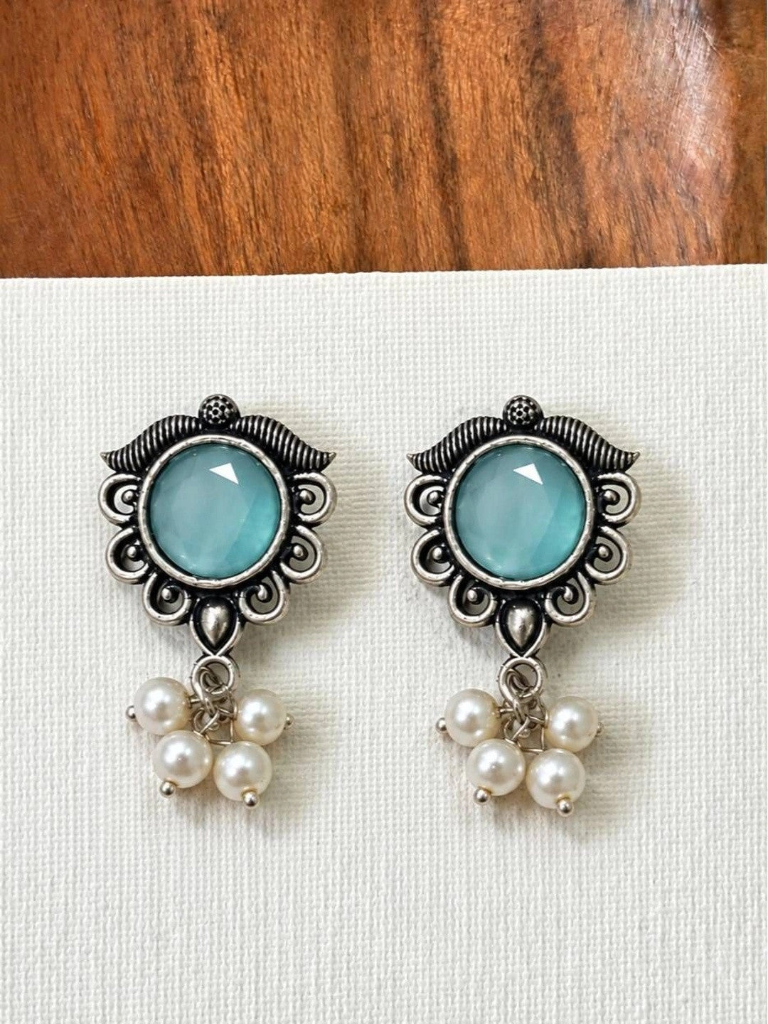 Two oxidised silver aqua stone earrings with pearl drops laid flat on white textured surface
