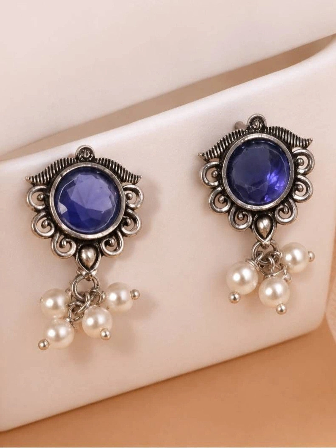 Pair of oxidised silver earrings with blue centre stones and pearl drops displayed on a white surface
