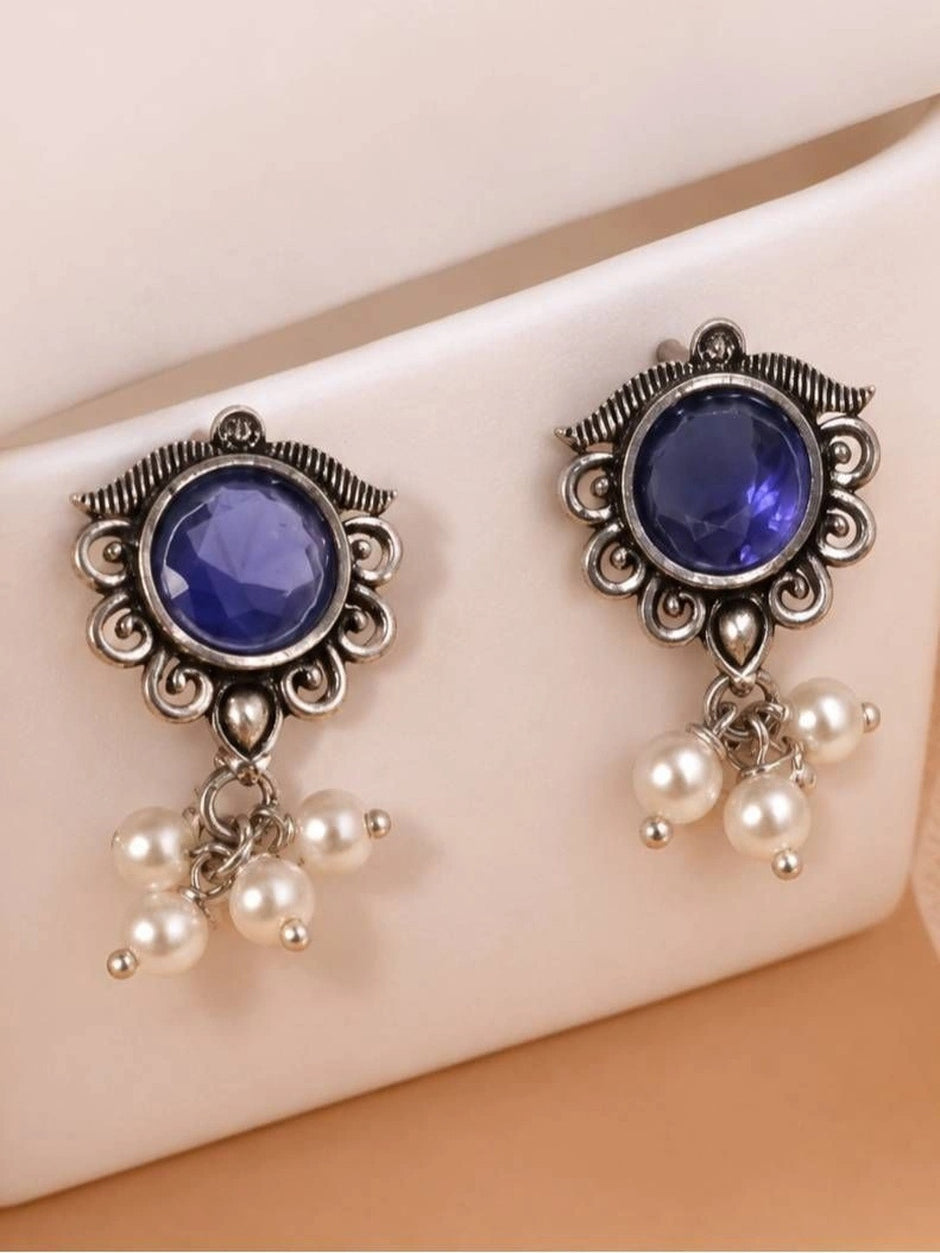 Pair of oxidised silver earrings with blue centre stones and pearl drops displayed on a white surface