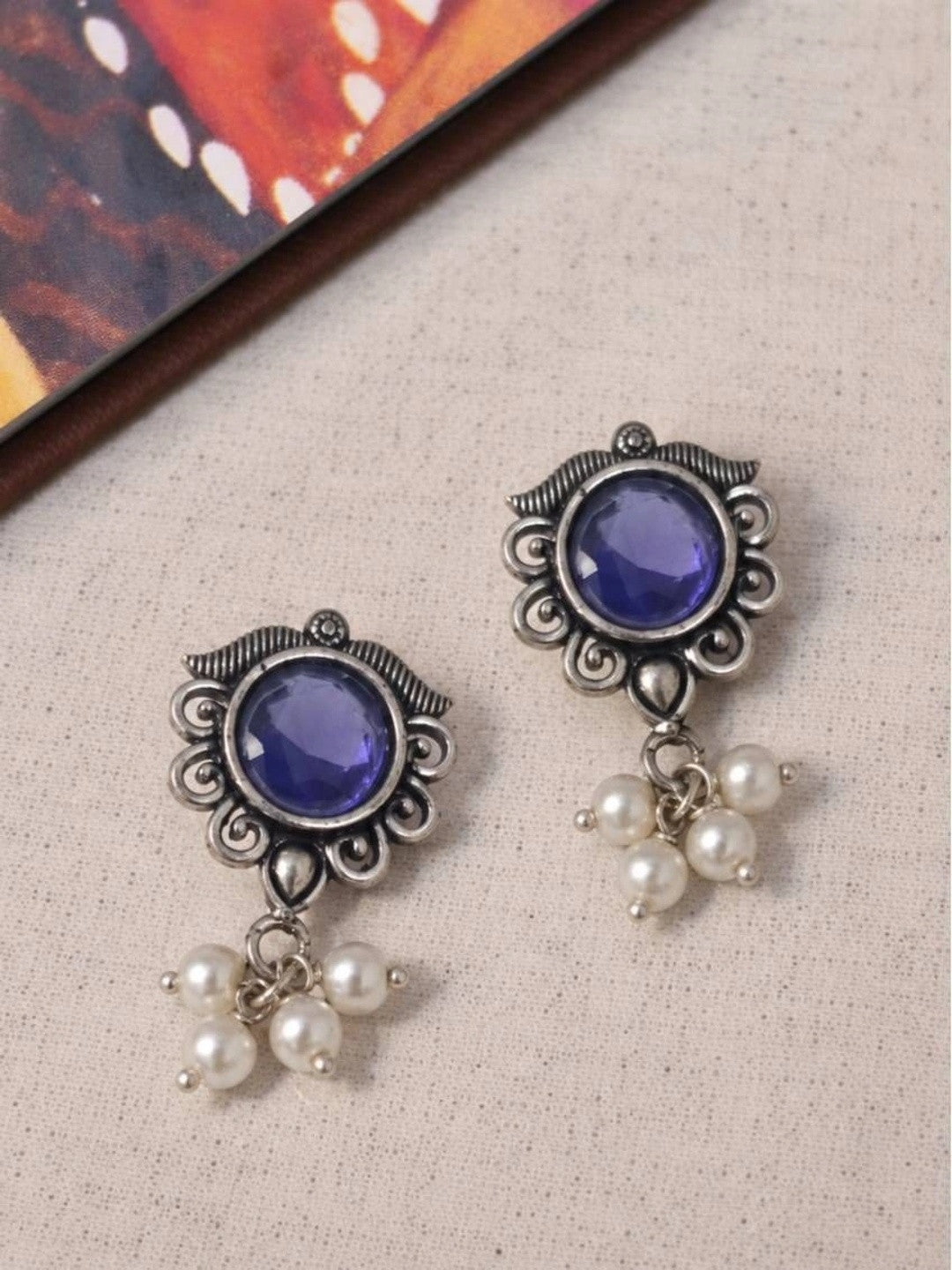 Two oxidised silver blue stone stud earrings with pearl drop clusters laid flat on a linen background