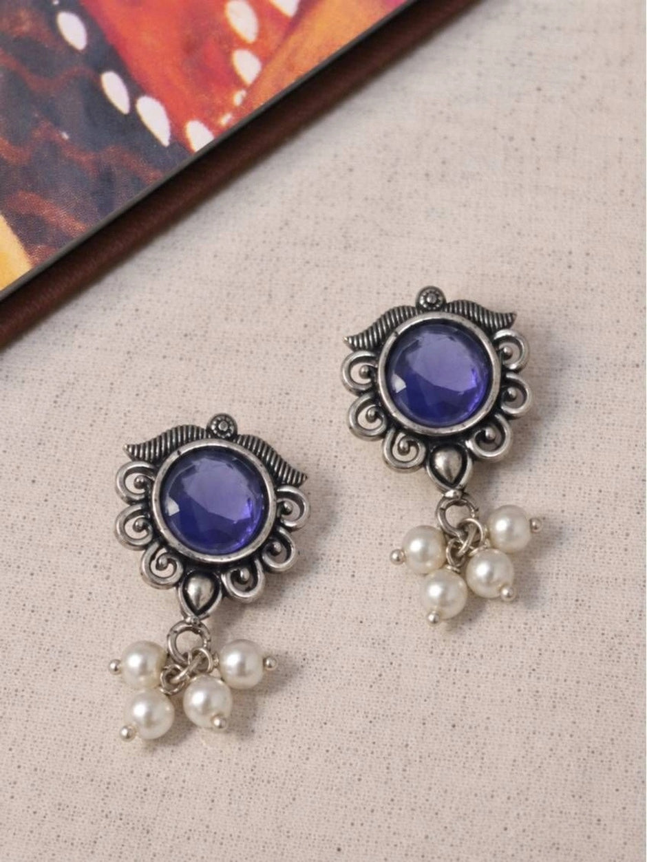 Two oxidised silver blue stone stud earrings with pearl drop clusters laid flat on a linen background