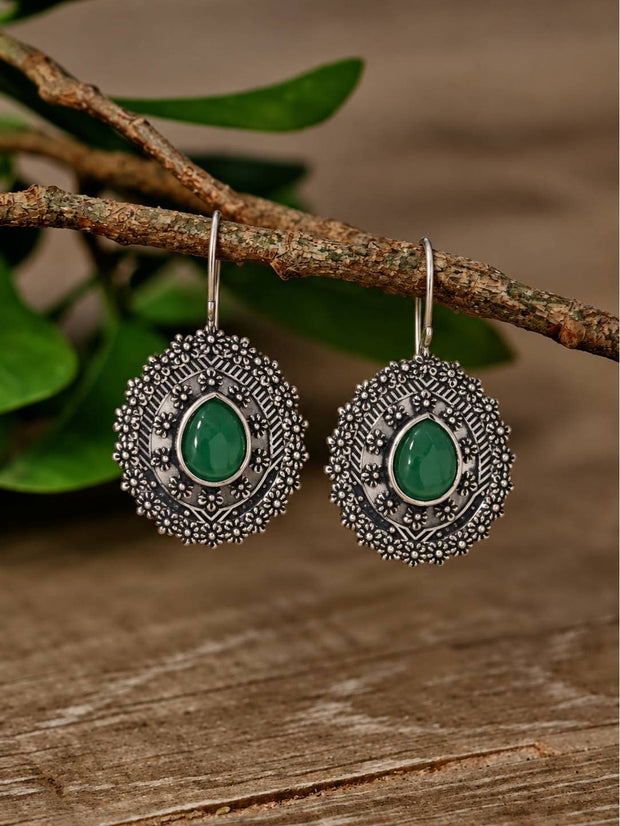 Pair of oxidised silver dome earrings with green teardrop stone hanging from a wooden branch