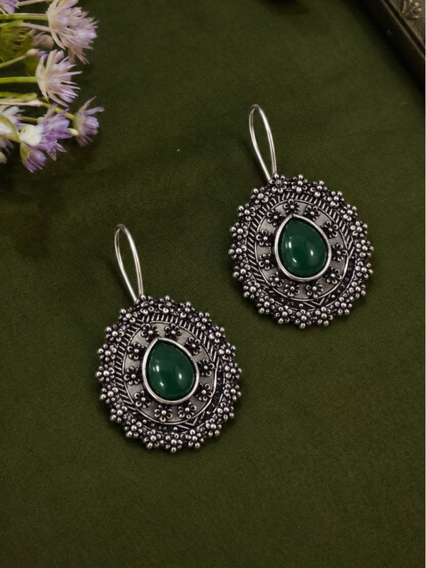 Front view of two oxidised silver floral dome earrings with green cabochon stones on green fabric