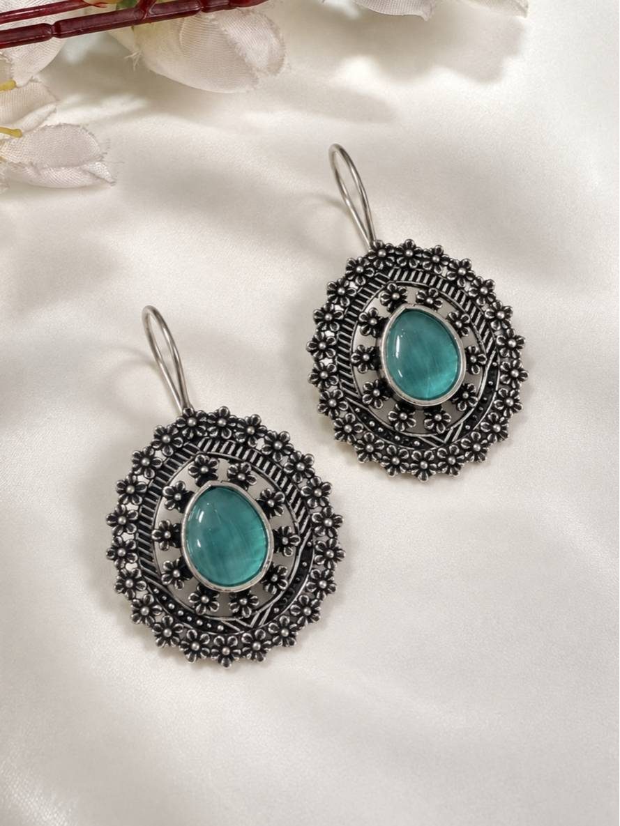 Front view of both oxidised silver floral disc earrings with turquoise stone on white satin fabric