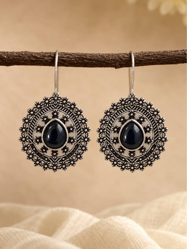 Pair of oxidised silver floral disc drop earrings with black teardrop cabochon hanging from a wooden branch