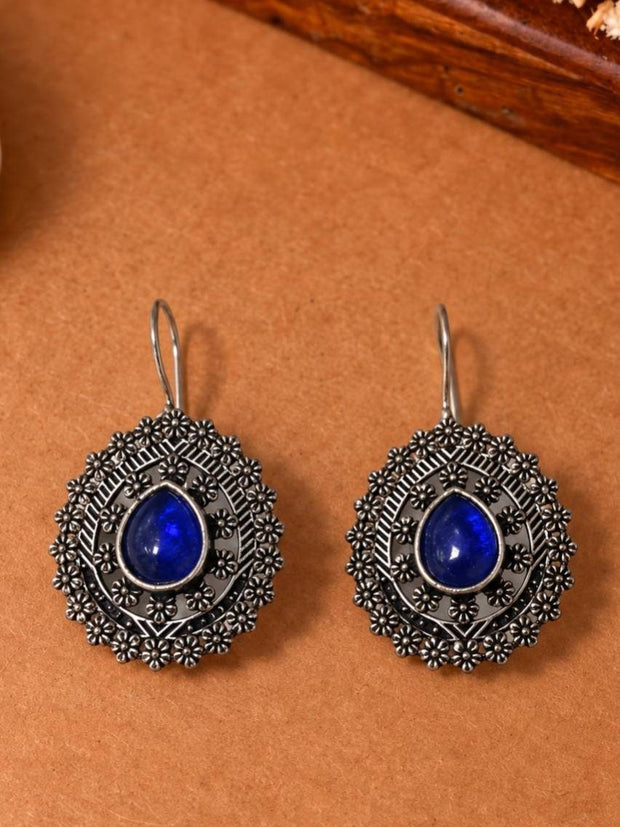 Front view of both oxidised silver blue stone drop earrings laid flat on a brown surface