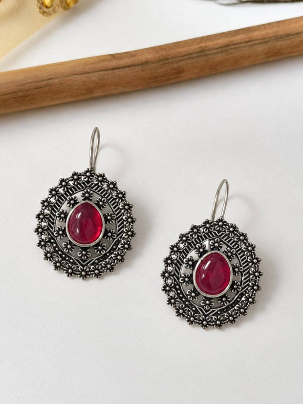 Two oxidised silver mandala drop earrings with red centre stone laid flat on a white surface