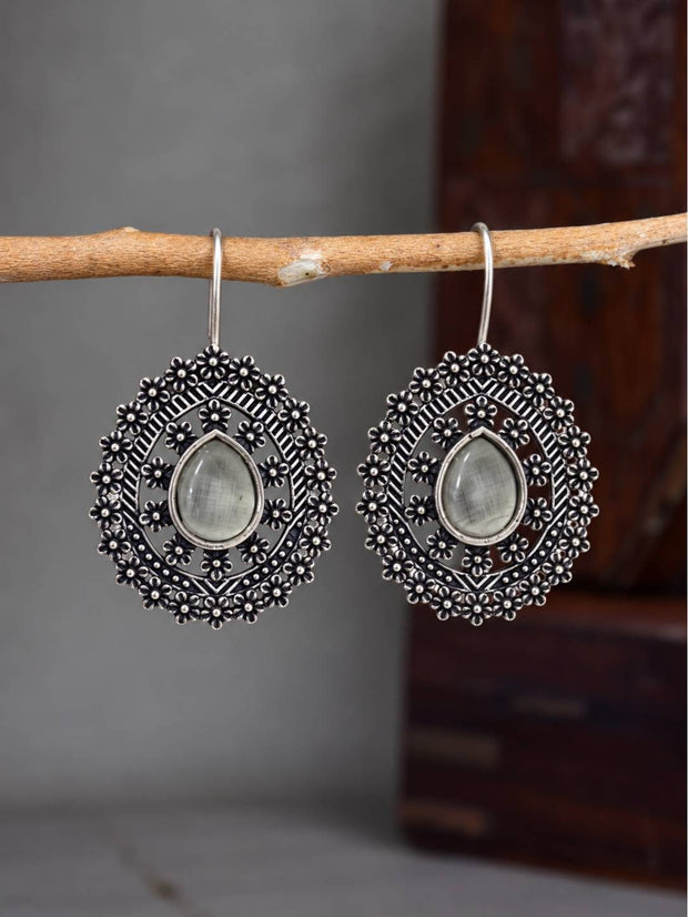 Pair of oxidised silver floral disc earrings with grey teardrop cabochon hanging from a wooden branch