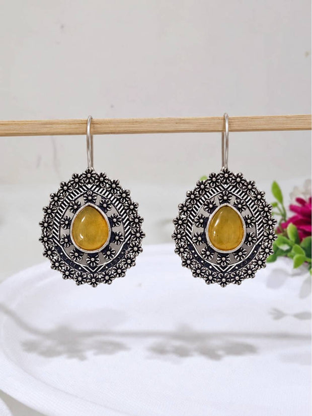 Pair of oxidised silver floral disc earrings with yellow teardrop cabochon, hanging on a wooden rod against a white background