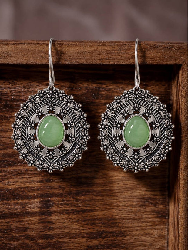 Pair of oxidised silver floral medallion drop earrings with green cabochon stones resting on a wooden tray