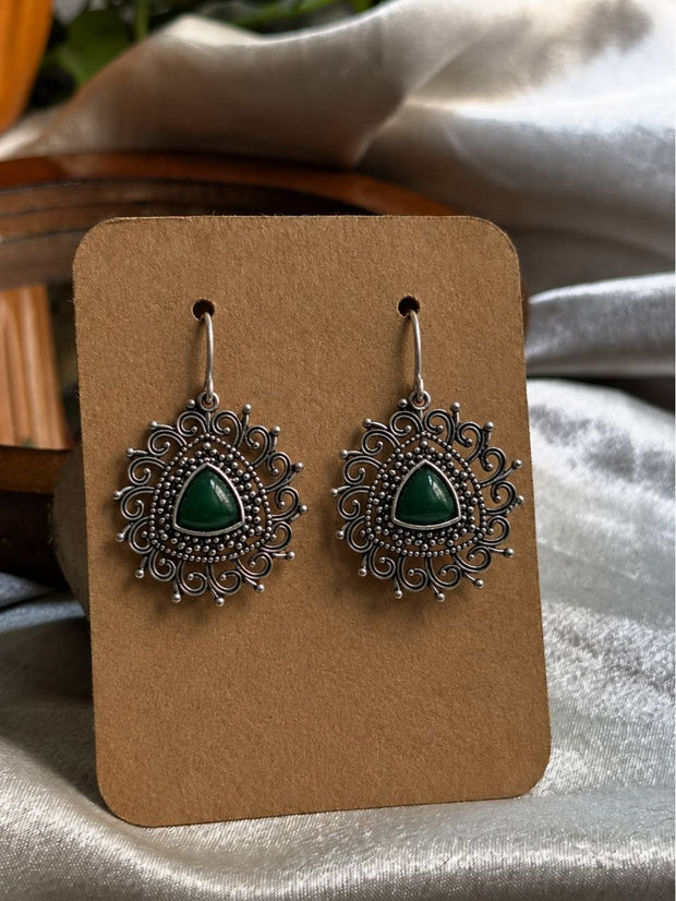 Pair of oxidised silver filigree drop earrings with green triangular stone on a kraft display card