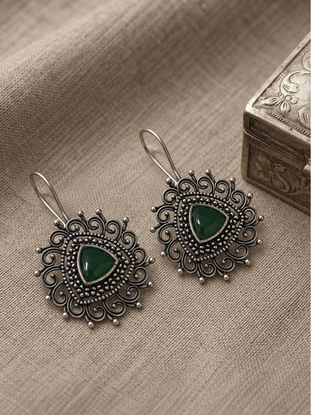Two oxidised silver earrings with green cabochon centres laid flat on linen fabric beside a silver box