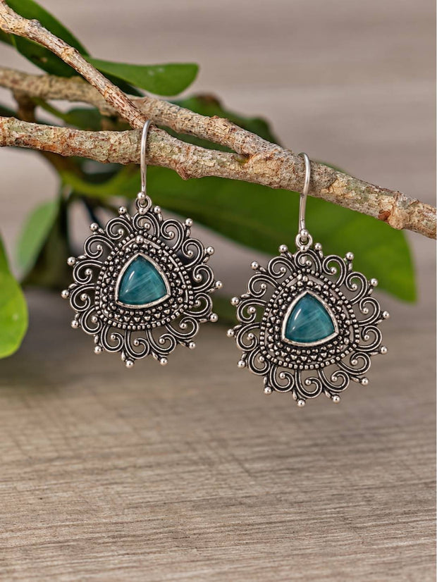 Pair of oxidised silver filigree dangle earrings with teal stone hung on a branch