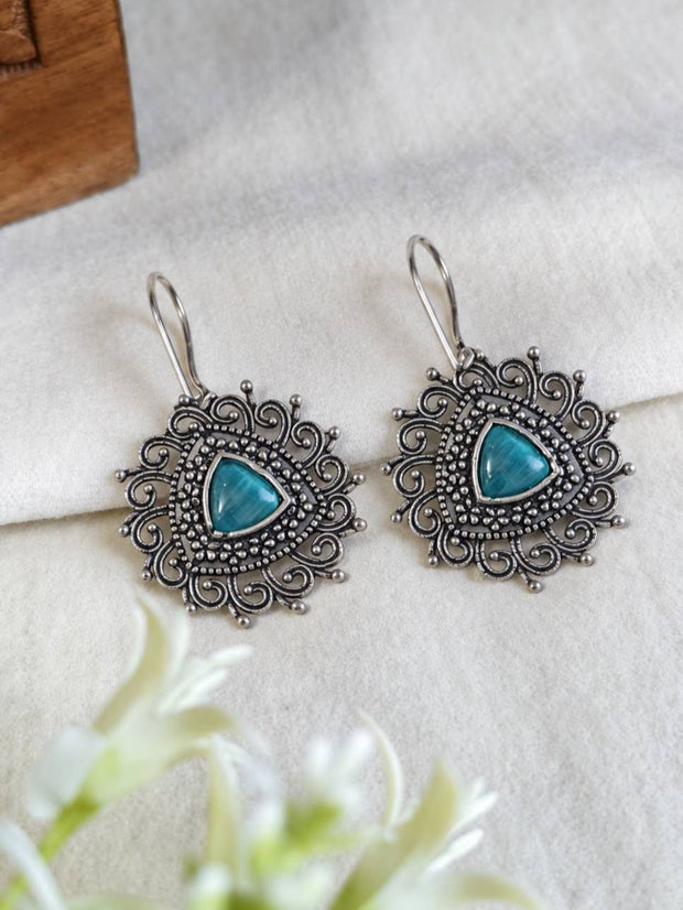 Front view of two oxidised silver mandala disc earrings with teal cabochon on white cloth