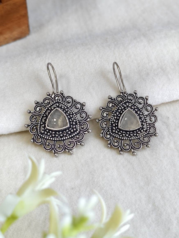Front view of both oxidised silver hook earrings with intricate swirl disc on white linen fabric