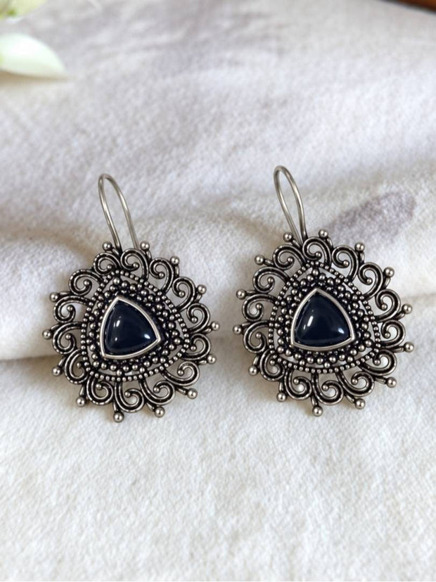 Two oxidised silver filigree drop earrings with black stone centres laid flat on white fabric