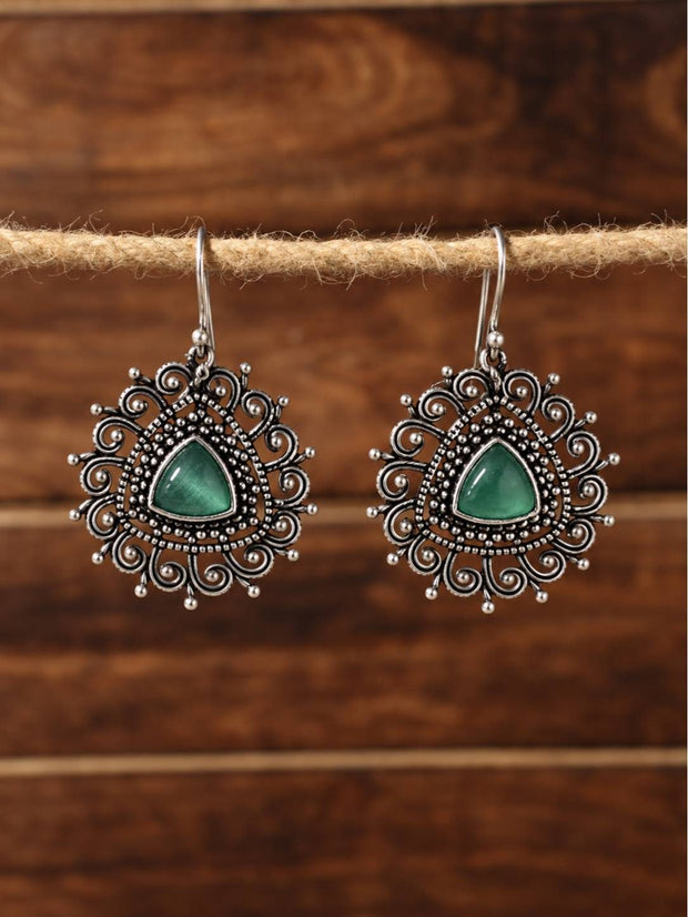 Pair of oxidised silver filigree drop earrings with green triangular stone hung on a jute rope against a wooden background