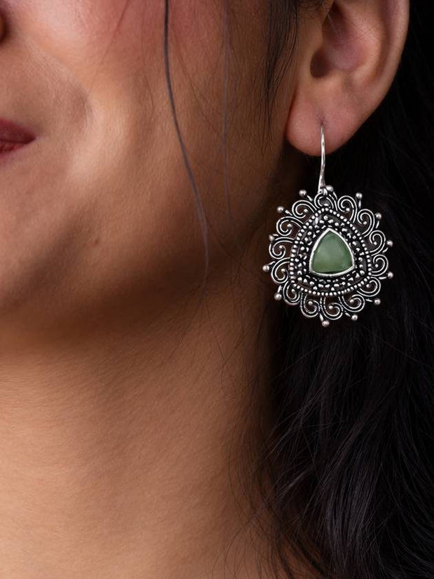 Model wearing an oxidised silver filigree drop earring with green stone on her left ear, shown in close-up profile view