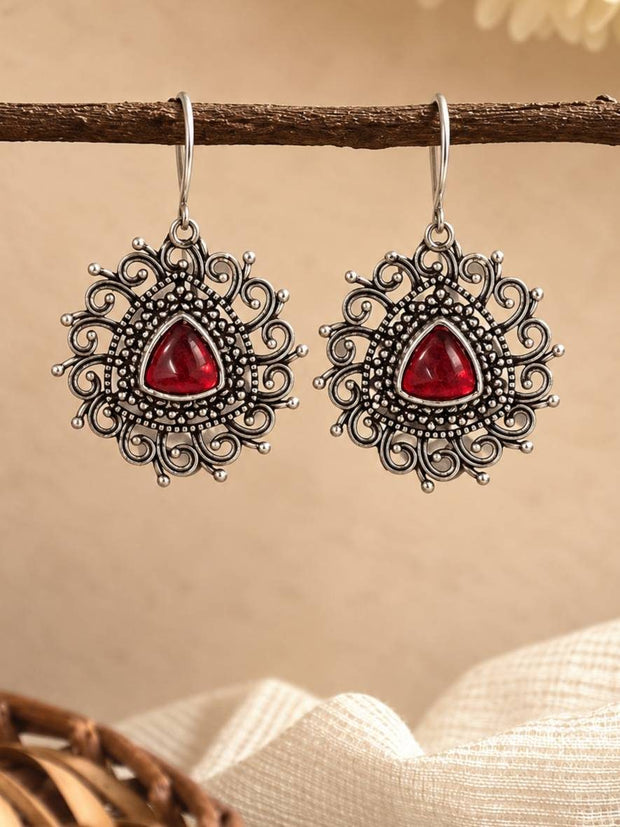 Pair of oxidised silver filigree drop earrings with red cabochon stone hanging from a wooden branch