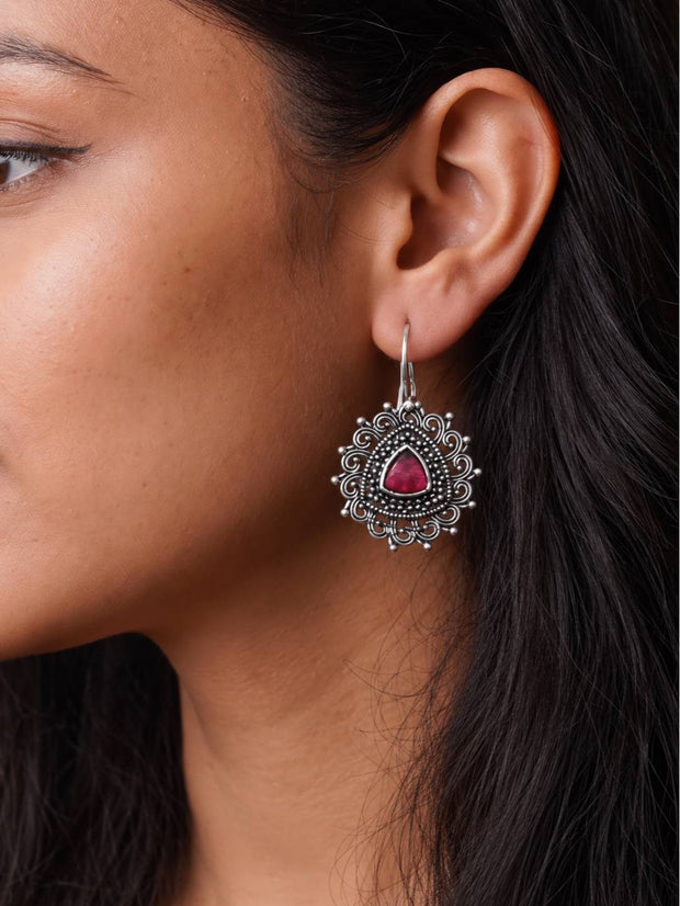 Woman wearing an oxidised silver filigree drop earring with red stone shown against dark hair