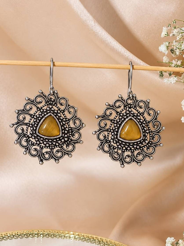 Pair of oxidised silver filigree drop earrings with amber cabochon stones hanging from a wooden rod against blush satin