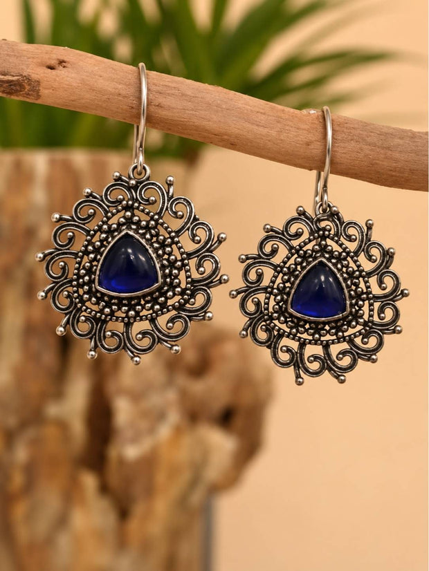 Pair of oxidised silver filigree drop earrings with blue cabochon stones hanging on a wooden branch