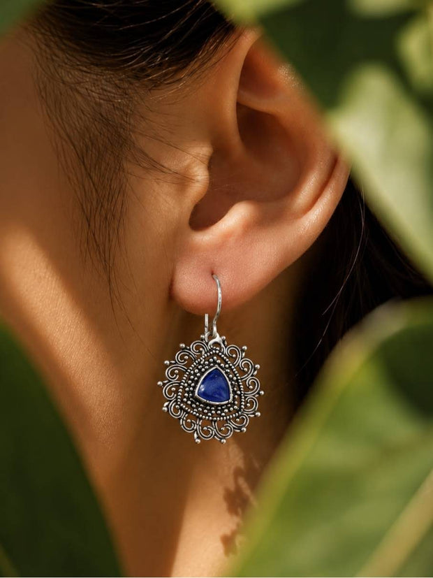 Oxidised silver filigree drop earring with blue stone worn on a woman's ear against green foliage