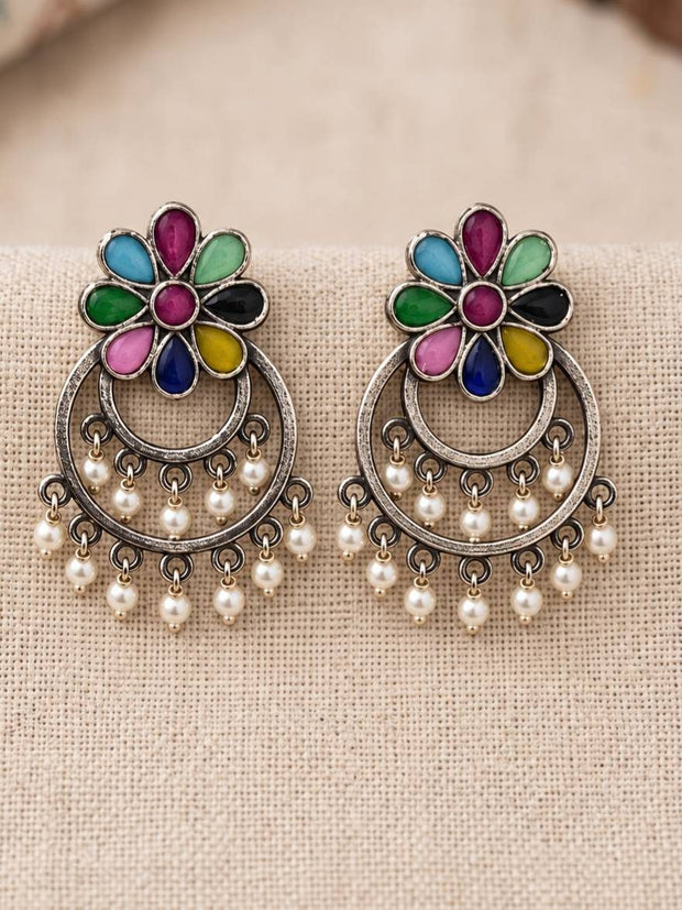 Pair of oxidised silver chandbali earrings with multicolour floral tops and white pearl drop dangles on a beige fabric surface