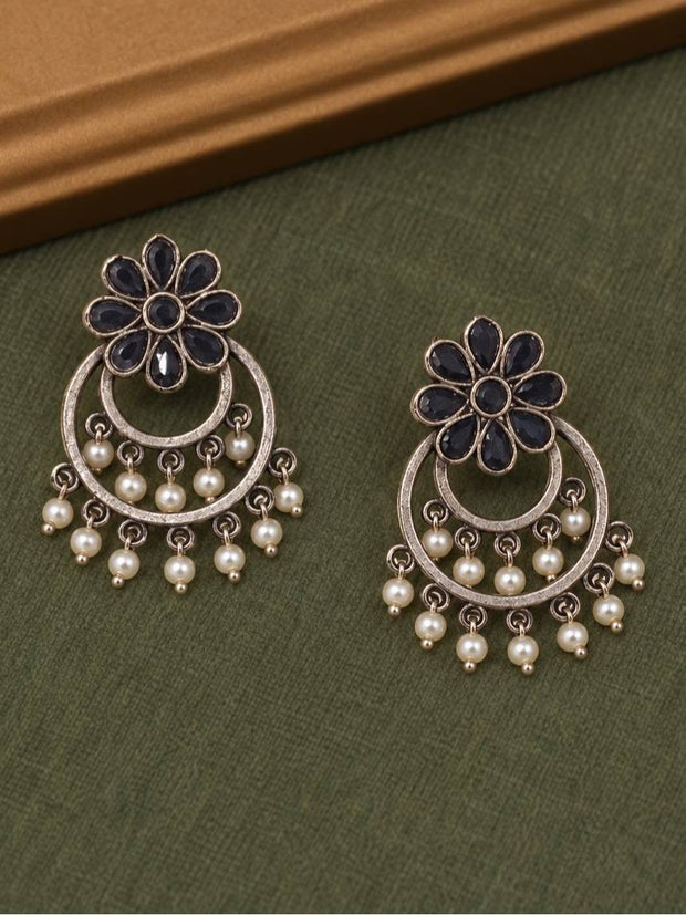 Front view of black stone floral chandbali earrings with pearl dangles laid flat on an olive green surface