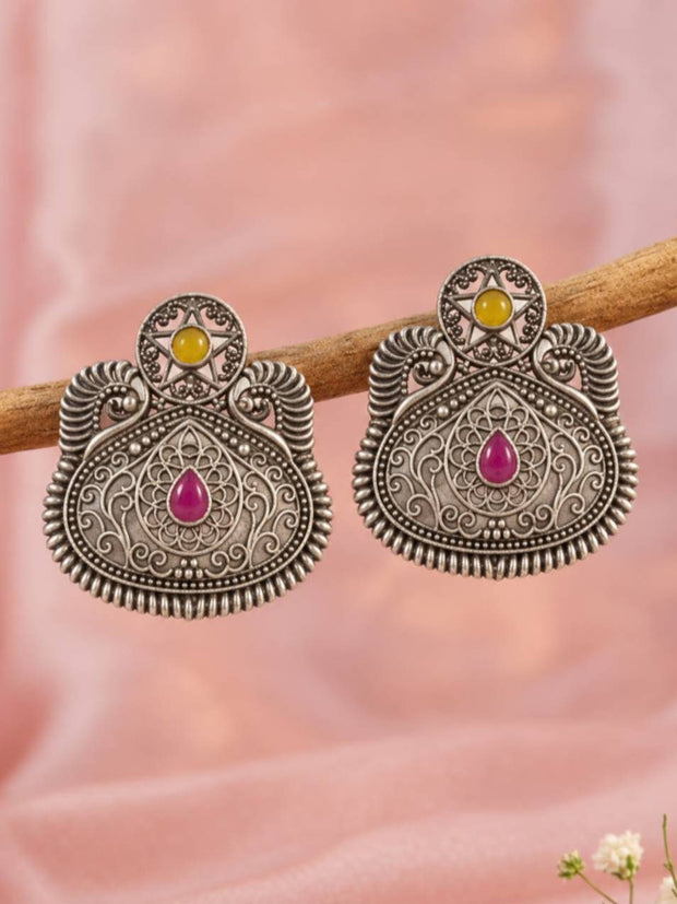 Pair of oxidised silver filigree stud earrings with pink teardrop and yellow star stones displayed on a wooden branch against pink fabric