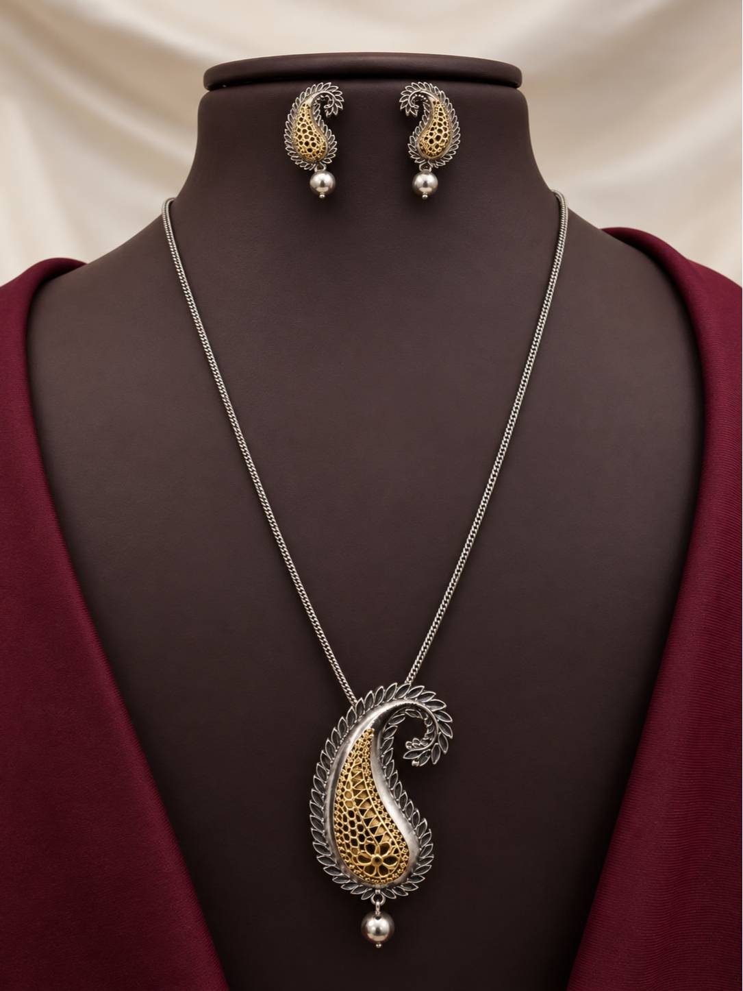 Dual-tone oxidised paisley pendant necklace and matching stud earrings displayed on a dark burgundy mannequin bust