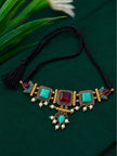 Antique gold turquoise and maroon stone choker necklace laid flat on dark green fabric with black dori cord and tassel