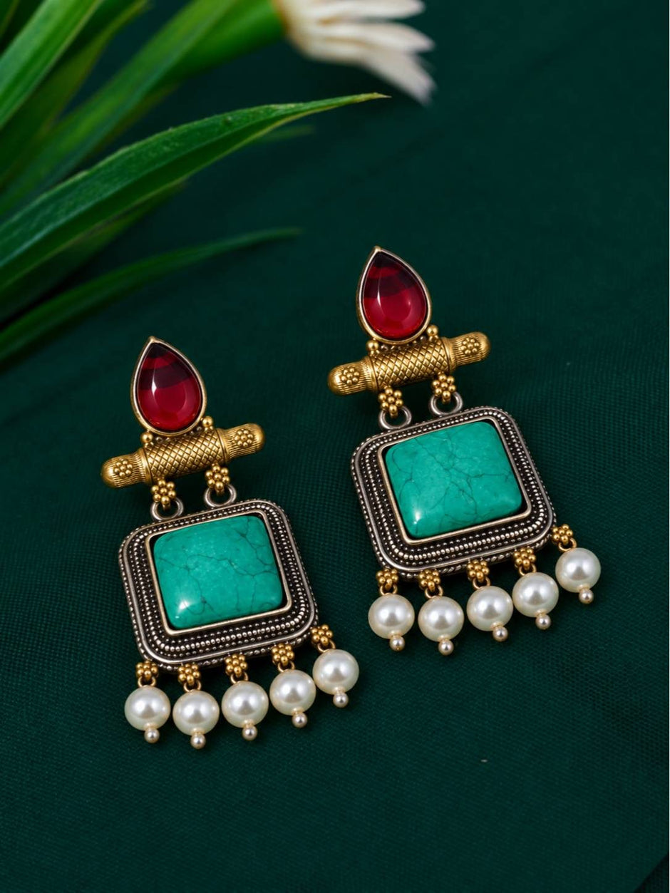 Close-up of a pair of antique gold turquoise square dangler earrings with maroon cabochon tops and pearl drops on green fabric