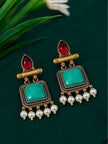 Close-up of a pair of antique gold turquoise square dangler earrings with maroon cabochon tops and pearl drops on green fabric