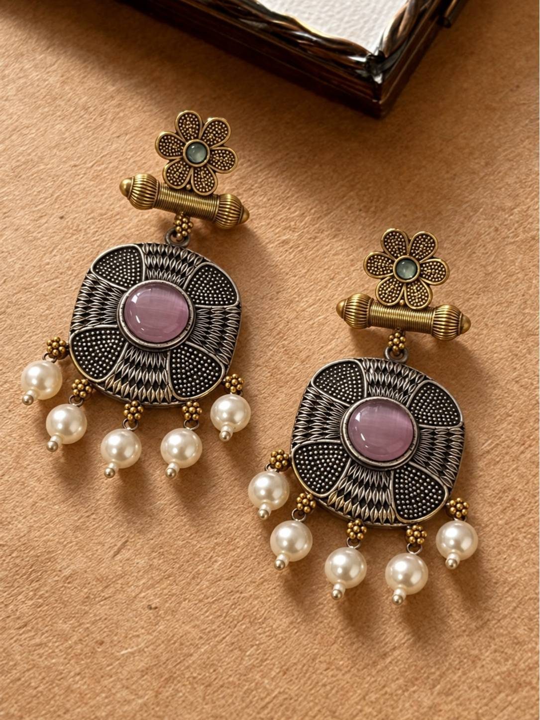 Close-up of oxidised antique gold and silver earrings with pink stone and pearl drops on a tan surface