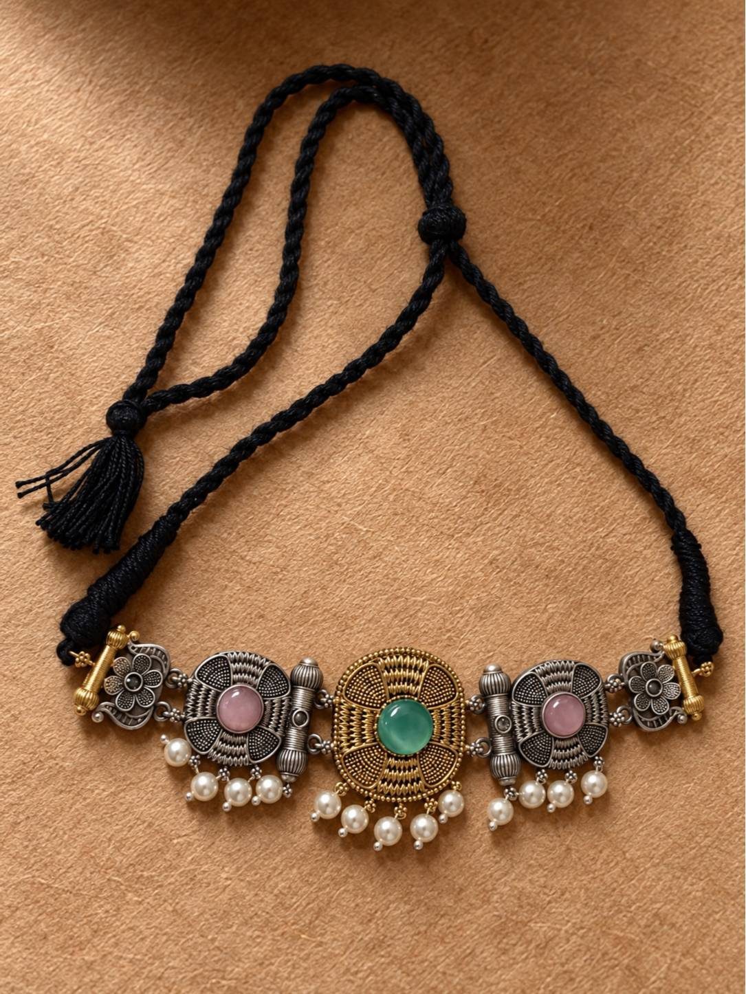 Flat lay of oxidised choker necklace on braided black dori with tassel closure on a tan background
