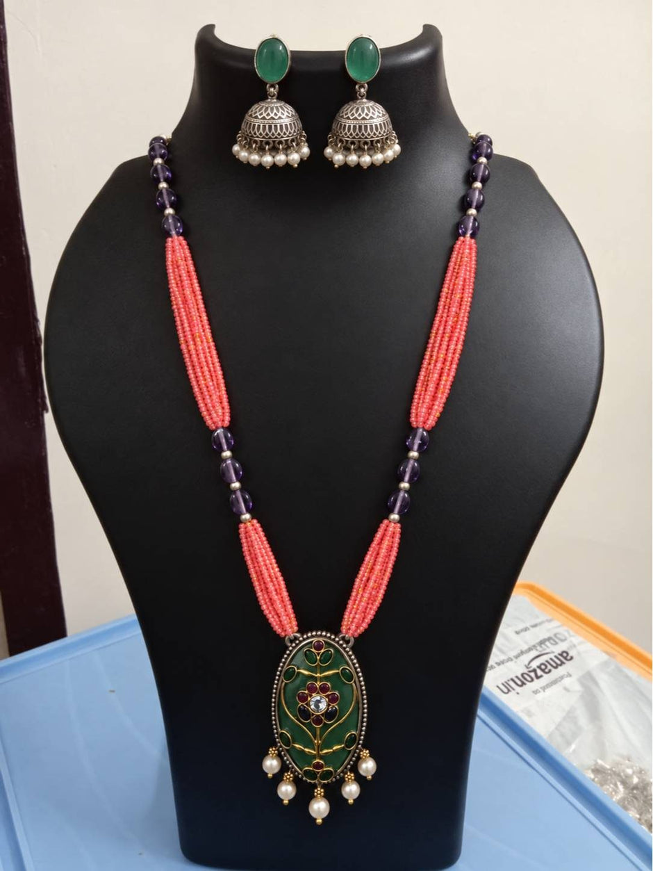 Coral bead meenakari pendant necklace and green cabochon jhumka earrings displayed on a black jewellery bust