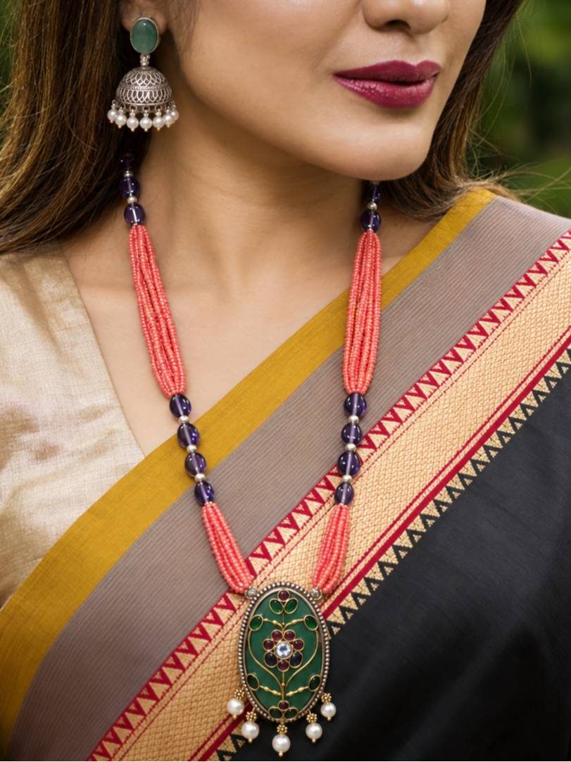 Model wearing coral bead meenakari necklace and jhumka earring with a black and gold silk saree