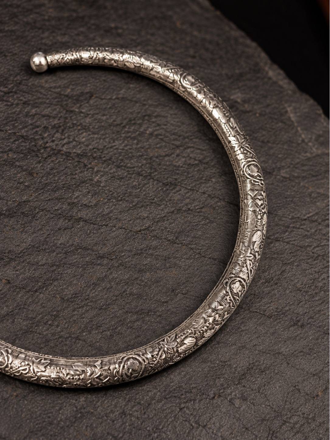 Close-up of hand-engraved floral motifs on oxidised silver brass choker necklace end terminal