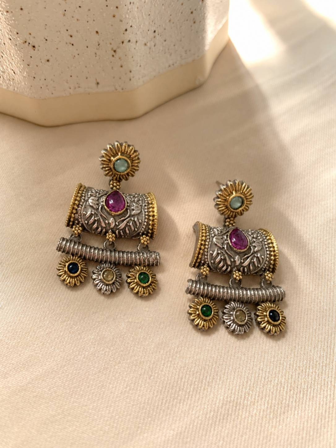 Close-up flat lay of a pair of oxidised dual-tone jhumka earrings with ruby, emerald and sapphire tone stones