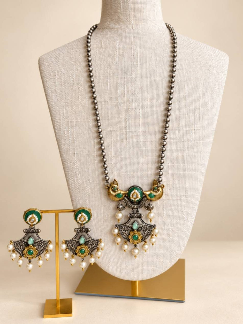 Oxidised dual-tone peacock necklace on bust form with matching chandbali earrings on gold stand