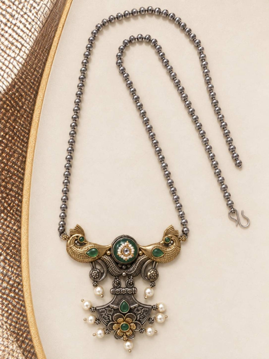 Flat lay of oxidised peacock pendant necklace with ball chain and hook clasp on cream background